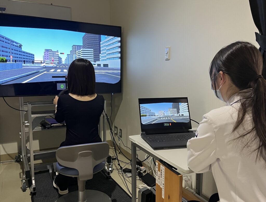 運転外来の様子。患者がドライビングシミュレーターを運転している様子を後ろから医師が観察している。